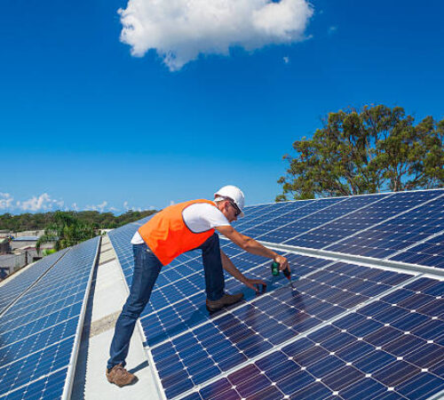 Young technician installing solar panels on factory roof